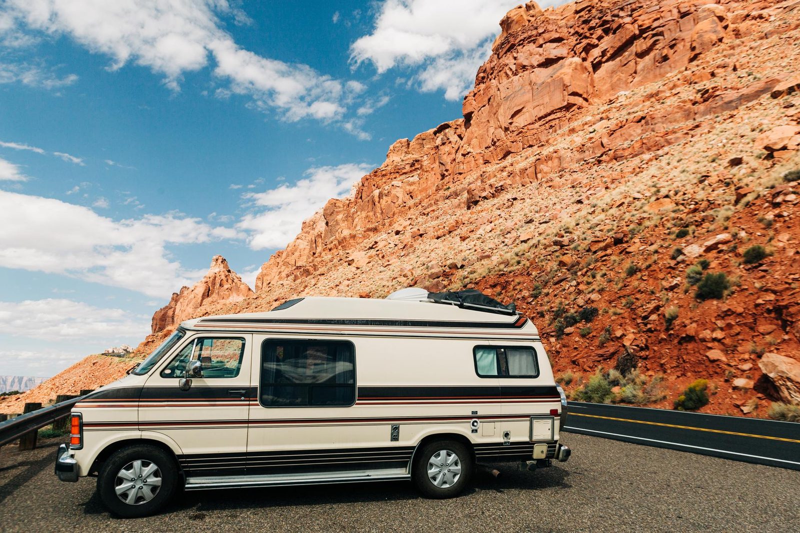 A cream high-top camper van parked at a roadside pullout below red cliffs near Marble Canyon, Arizona
