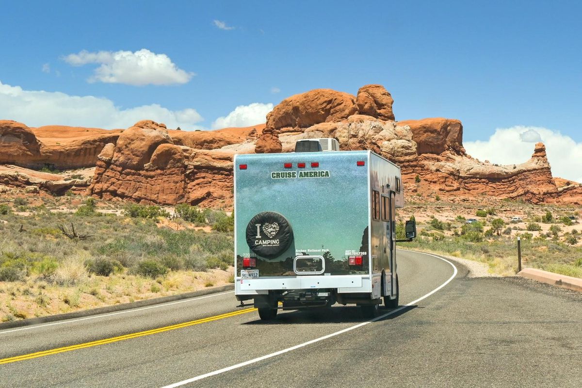 A rental Class C motorhome seen from behind on a desert highway between red rock formations