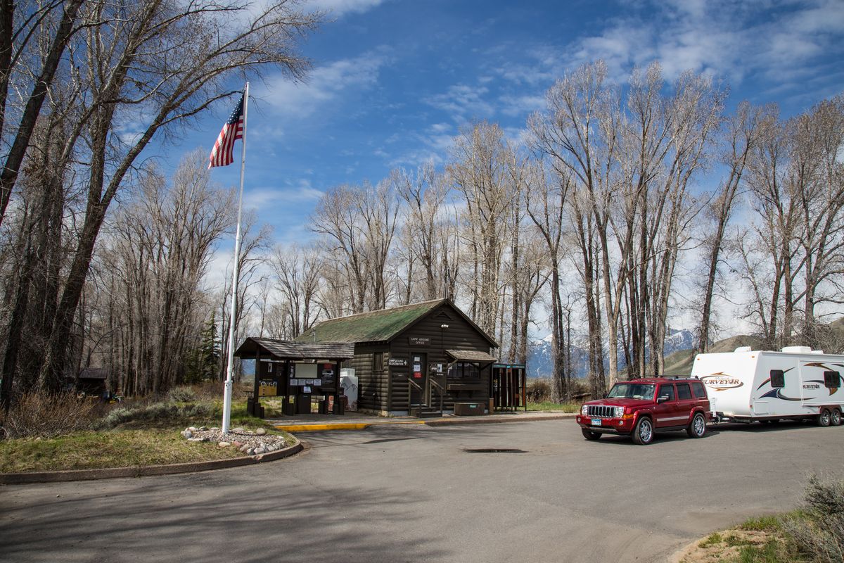 A pickup and a travel trailer parked by the log office at the entrance to Gros Ventre Campground, Grand Teton National Park, under bare cottonwoods