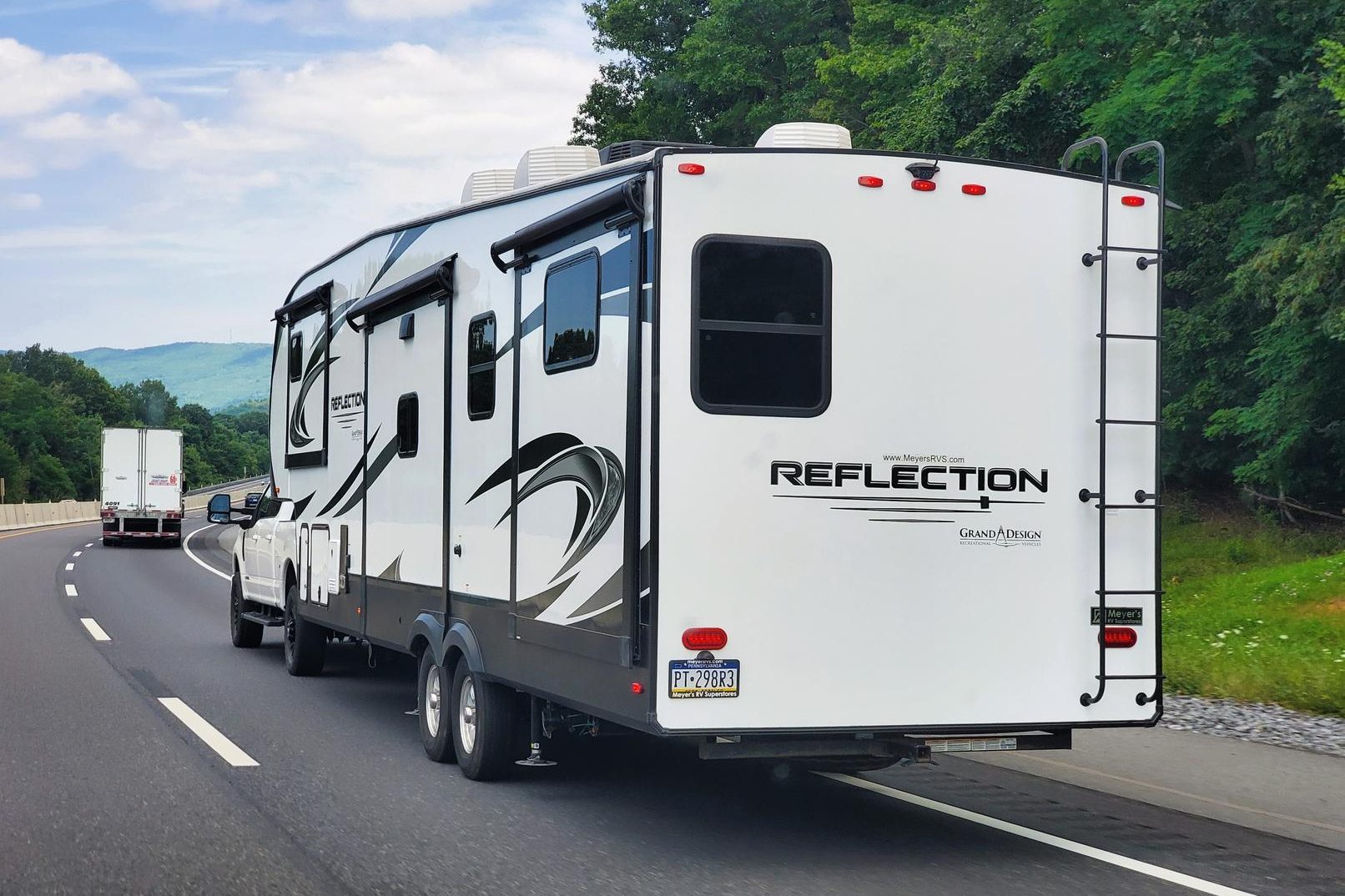 A pickup towing a large travel trailer on a tree-lined highway