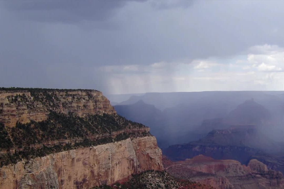 A rain shower moving across the Grand Canyon below a grey sky