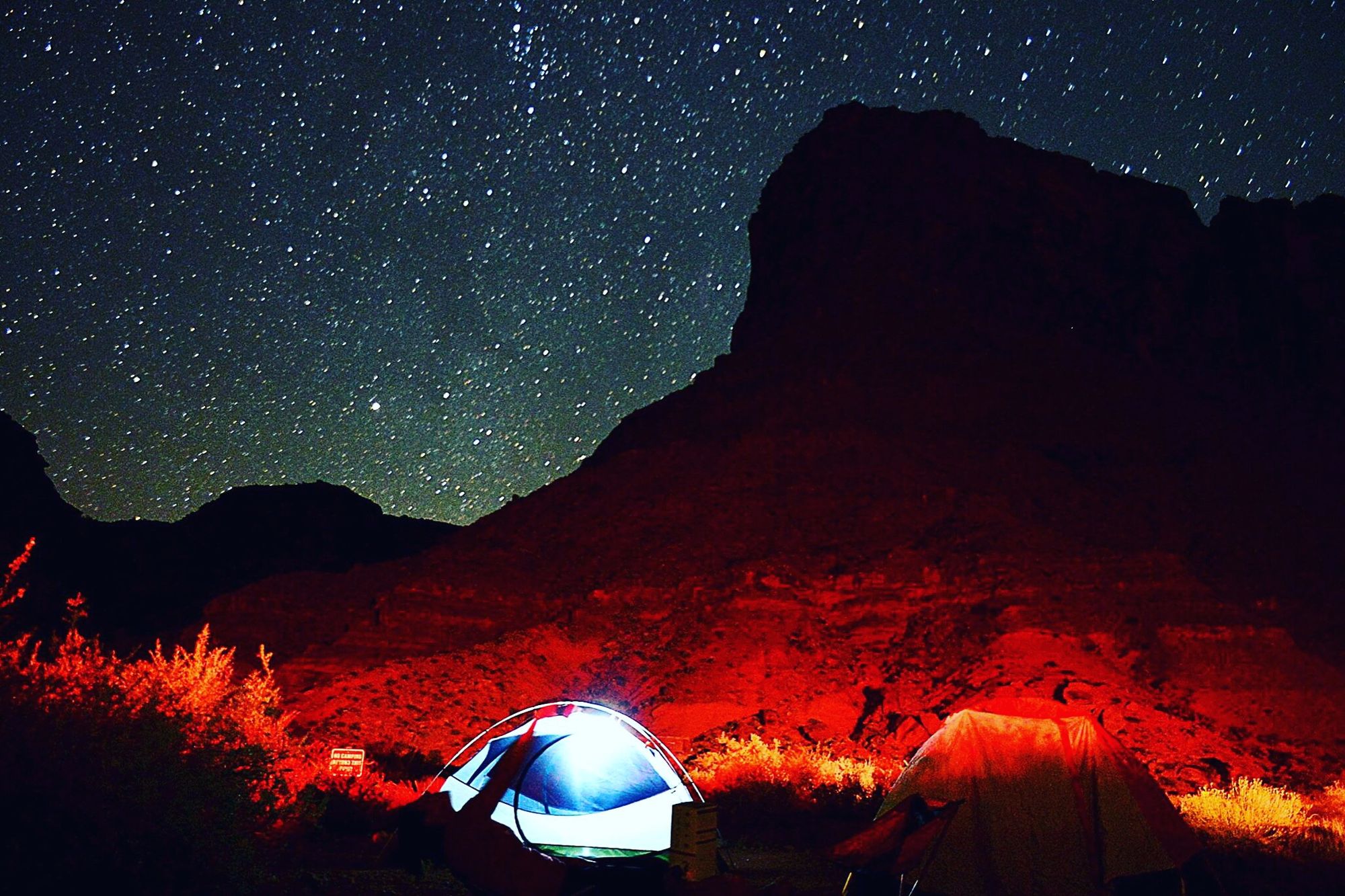 Two lit tents below a dark sandstone butte under a starry sky at Big Bend Campground, a BLM campground on the Colorado River near Moab