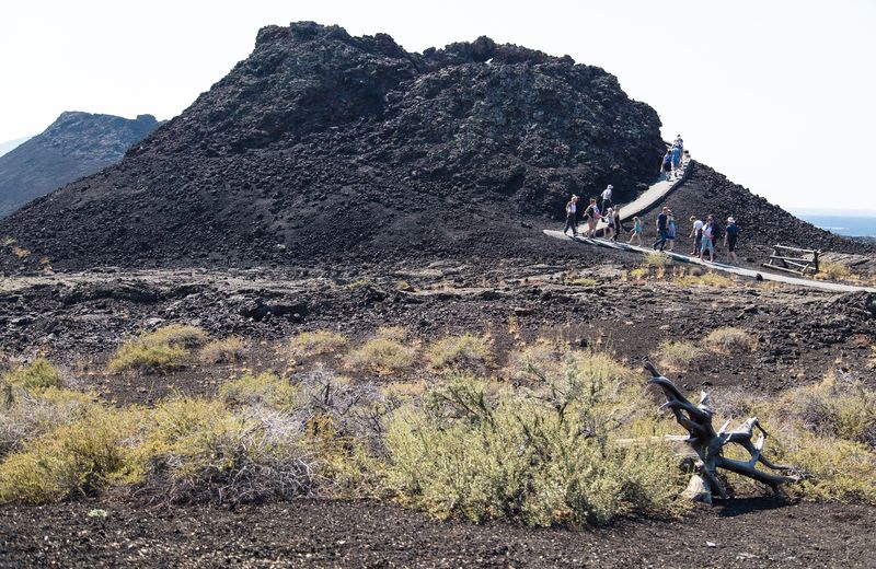 A paved trail across black lava past a dark spatter cone at Craters of the Moon, Idaho