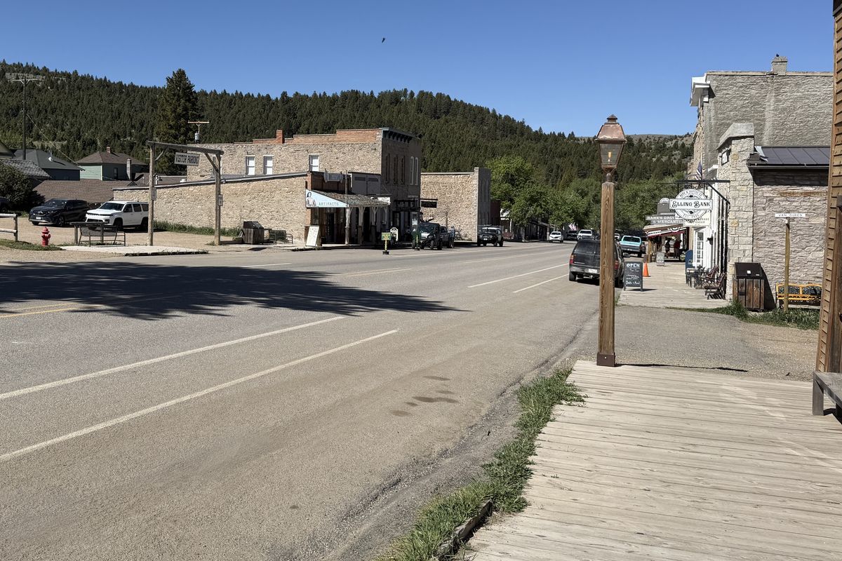 Wallace Street in Virginia City, Montana: old buildings and a wooden boardwalk along the paved highway, with forested hills behind