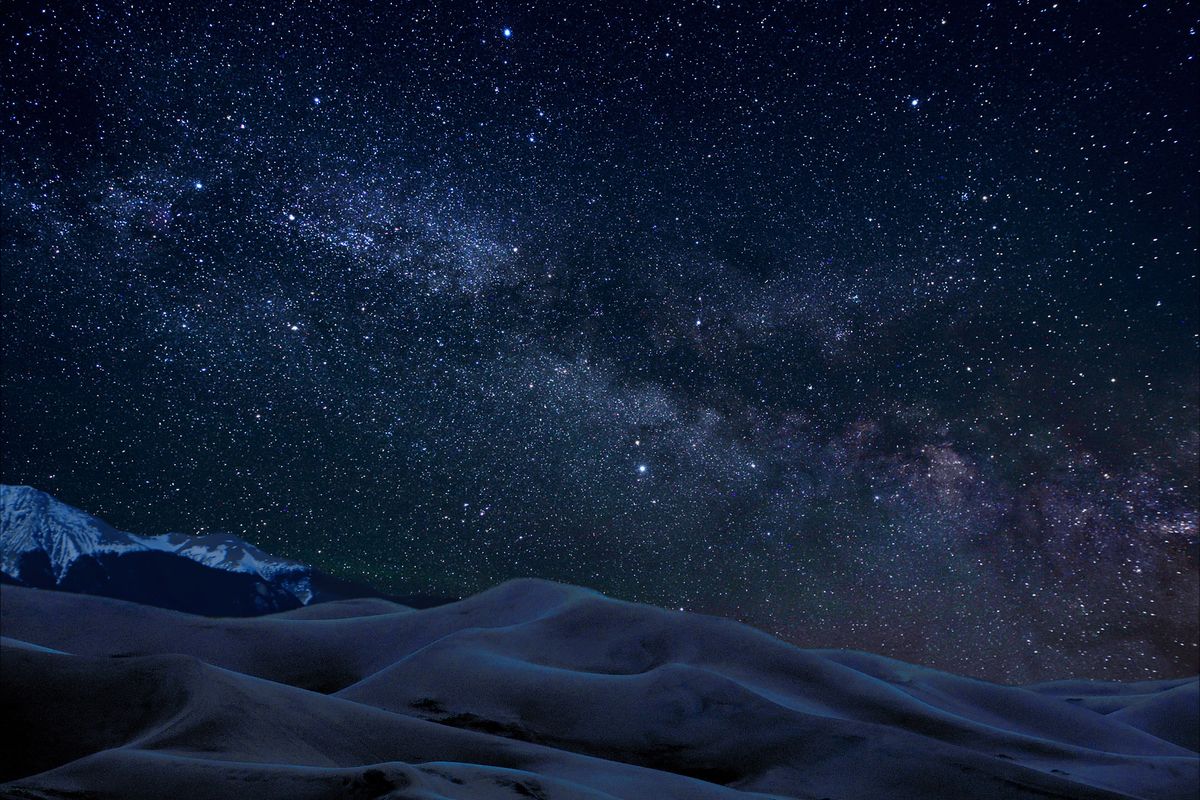 The Milky Way in a star-filled night sky above the dark curves of the sand dunes