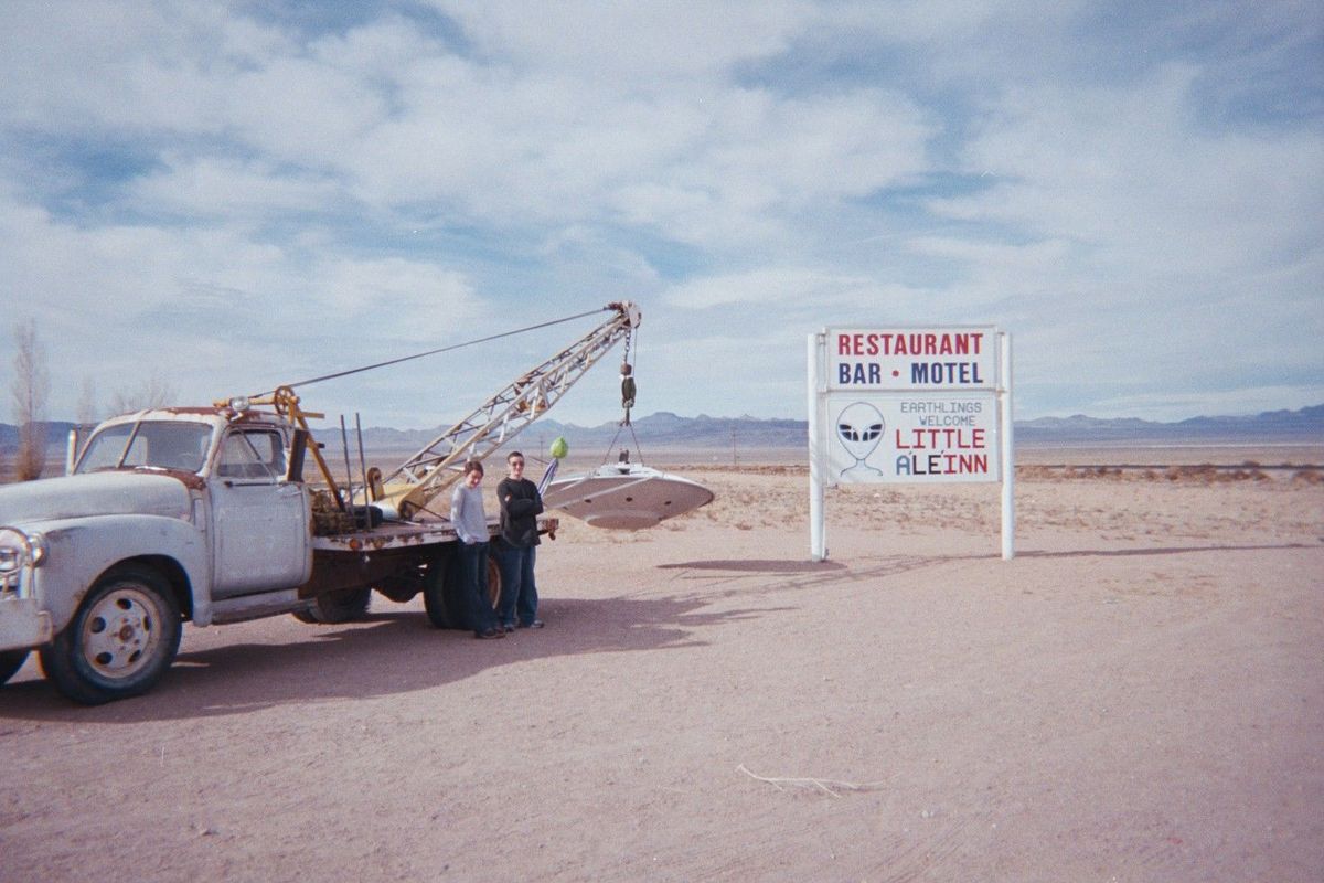 The Little A'Le'Inn roadside sign in Rachel, Nevada, next to an old tow truck dangling a model flying saucer from its crane, desert behind