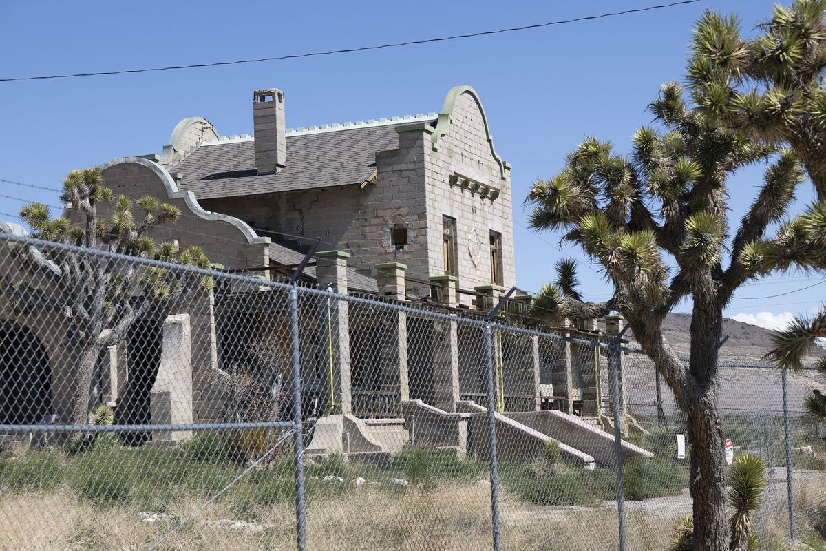 The Mission-style Rhyolite train depot behind a wire fence with Joshua trees in the foreground