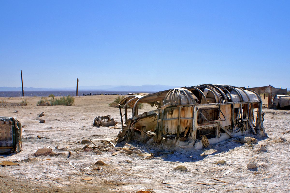 The rusted, roofless frame of an old trailer and other debris half-buried in salt-crusted ground on the former shore at Bombay Beach