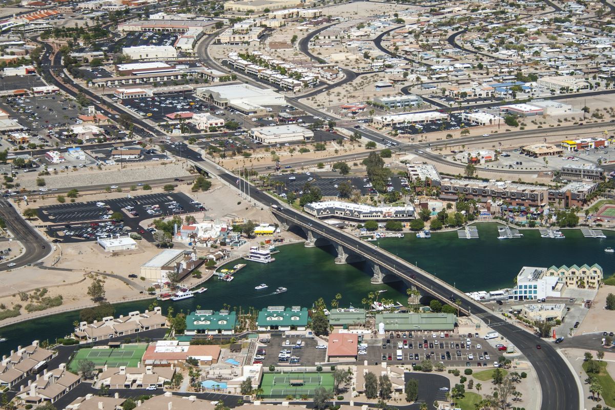 Aerial view of Lake Havasu City: a stone bridge crossing a narrow blue channel, with boats, a marina, streets and buildings on both sides