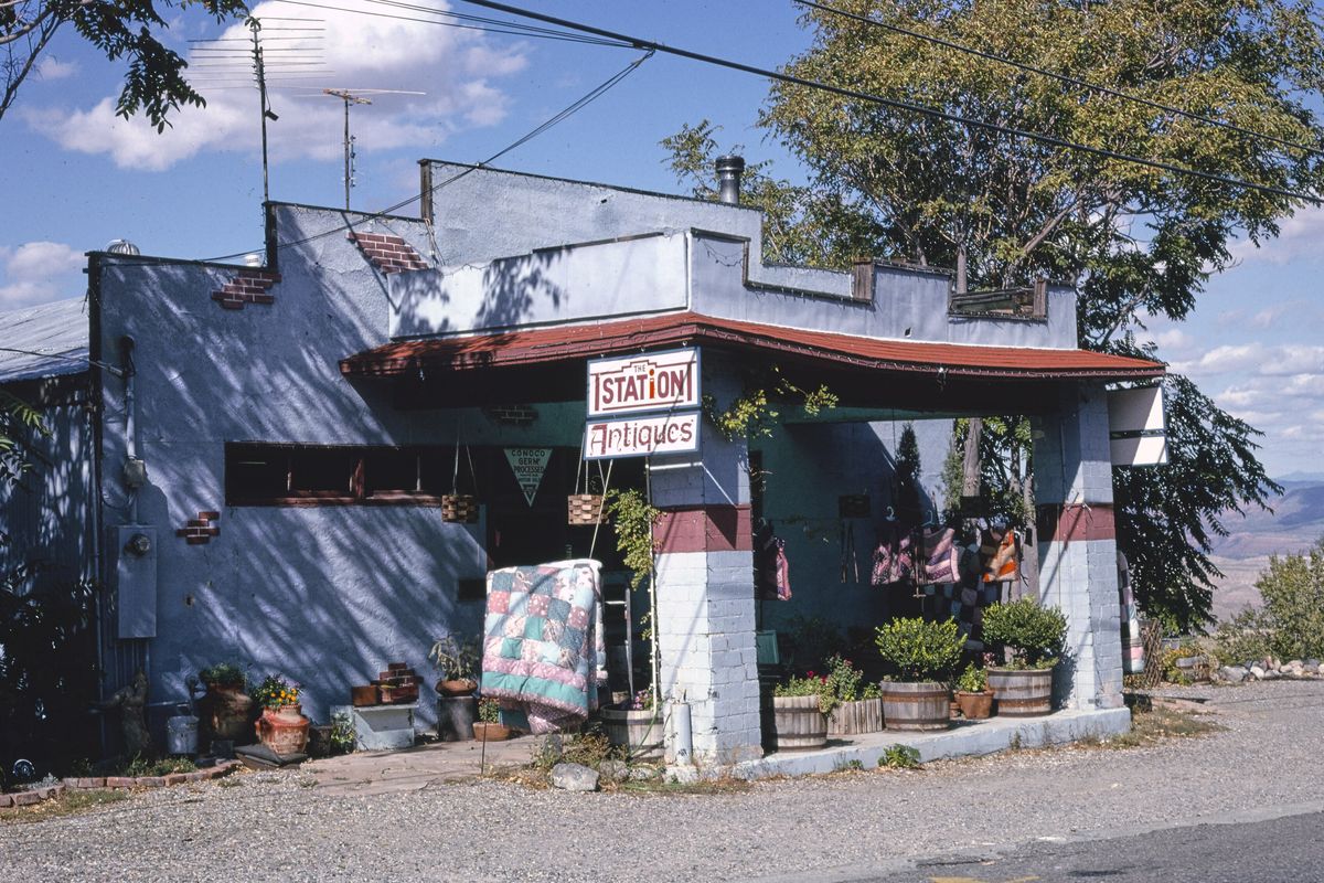 An old gas station turned antiques shop in Jerome, Arizona, with a quilt and potted plants outside and the Verde Valley in the distance