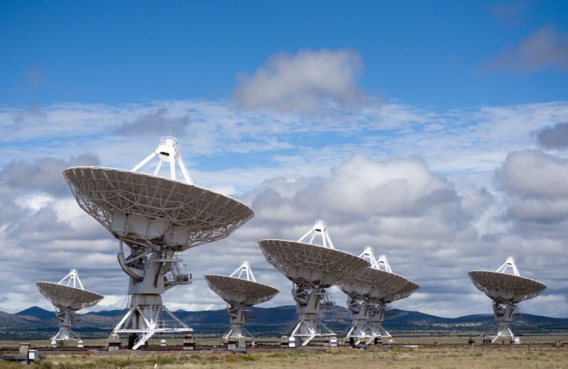 White radio telescope dishes of the Very Large Array on a plain in New Mexico under a cloudy blue sky