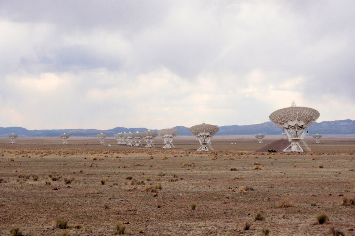 Radio telescope dishes of the Very Large Array spread across the flat, dry Plains of San Agustin, one large dish closer to the camera