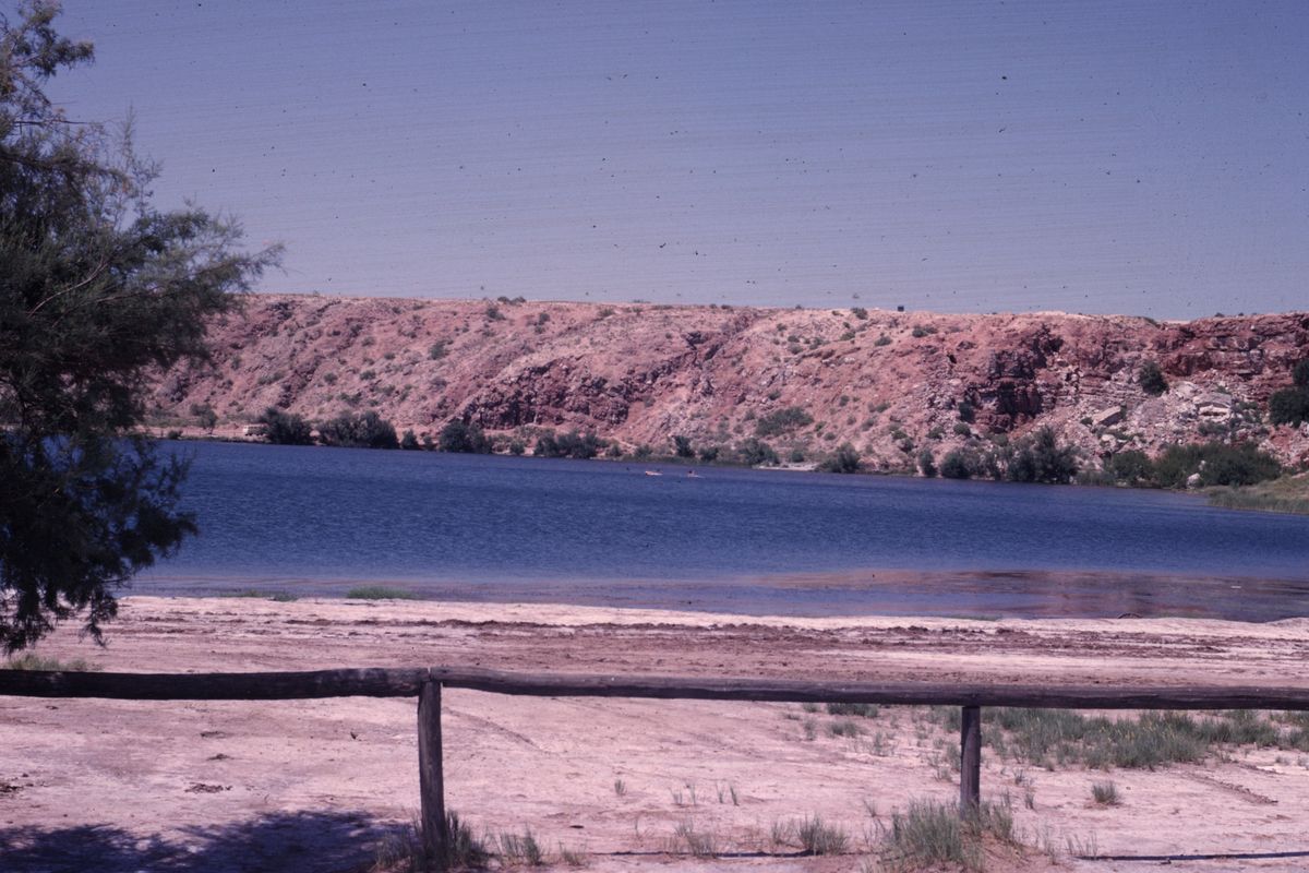 A lake below reddish bluffs at Bottomless Lakes State Park near Roswell, with a wooden fence on the pale shore