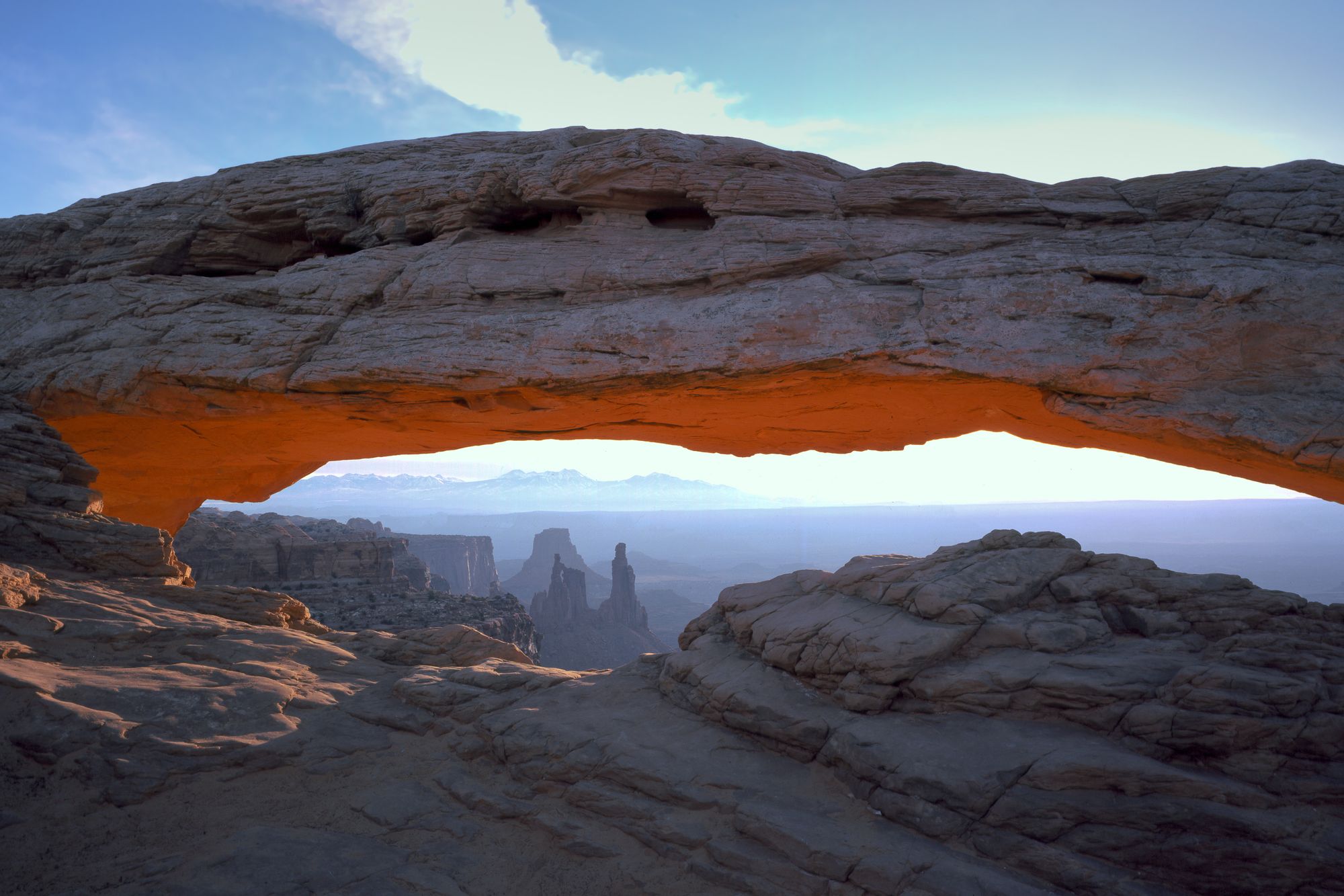 Mesa Arch glowing orange on its underside at sunrise, with canyons and distant mountains beyond, Island in the Sky, Canyonlands National Park